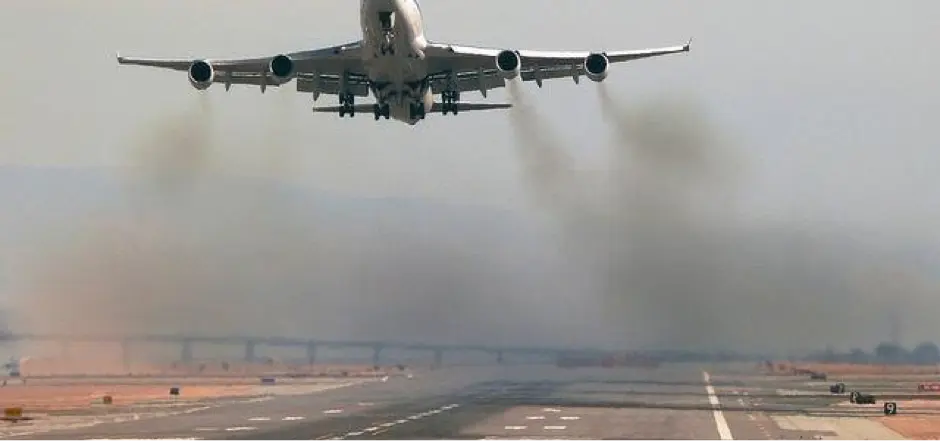 A jet airliner taking off, trailing dark exhaust over the runway