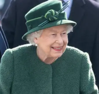 Queen Elizabeth II, smiling, in a green coat and hat