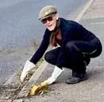 Trilby Roberts, in gardening gloves and a cap, clearing a roadside gutter